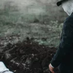 Bloody murderer stands against a grave with victim